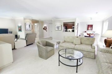 A modern living room with a sofa, chair, and glass coffee table, decorated with artwork.