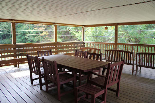 A spacious outdoor dining area with wooden furniture on a covered porch.