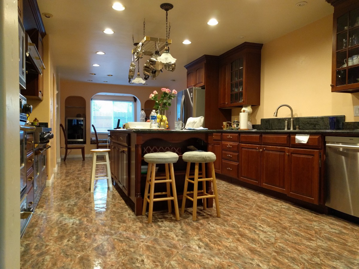 A spacious kitchen featuring an island with bar stools, wood cabinetry, and a chandelier.