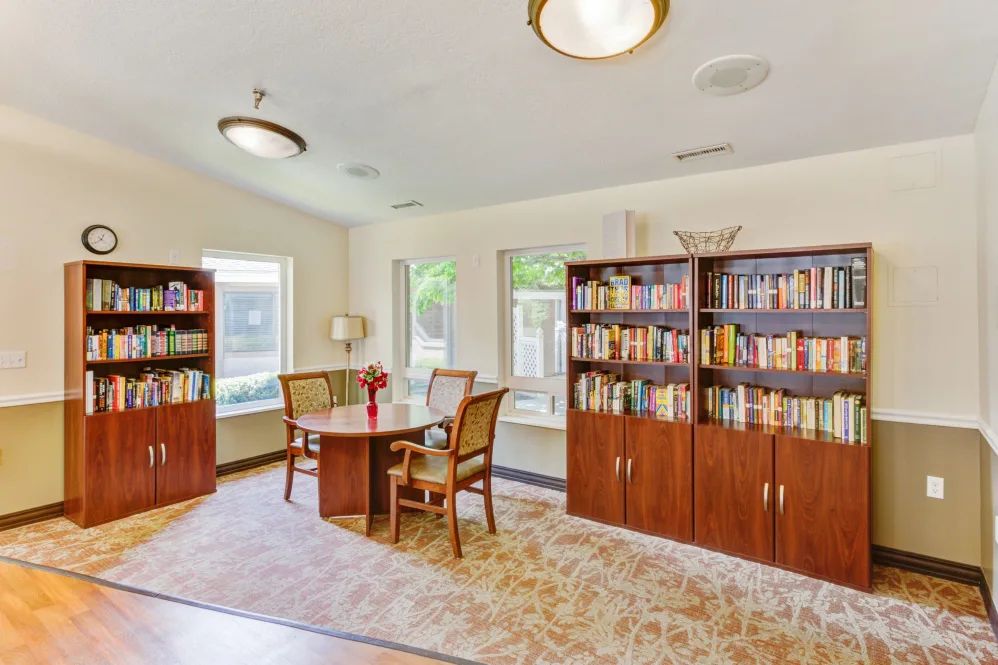 A cozy library space with bookshelves, a reading table, and chairs by the windows.