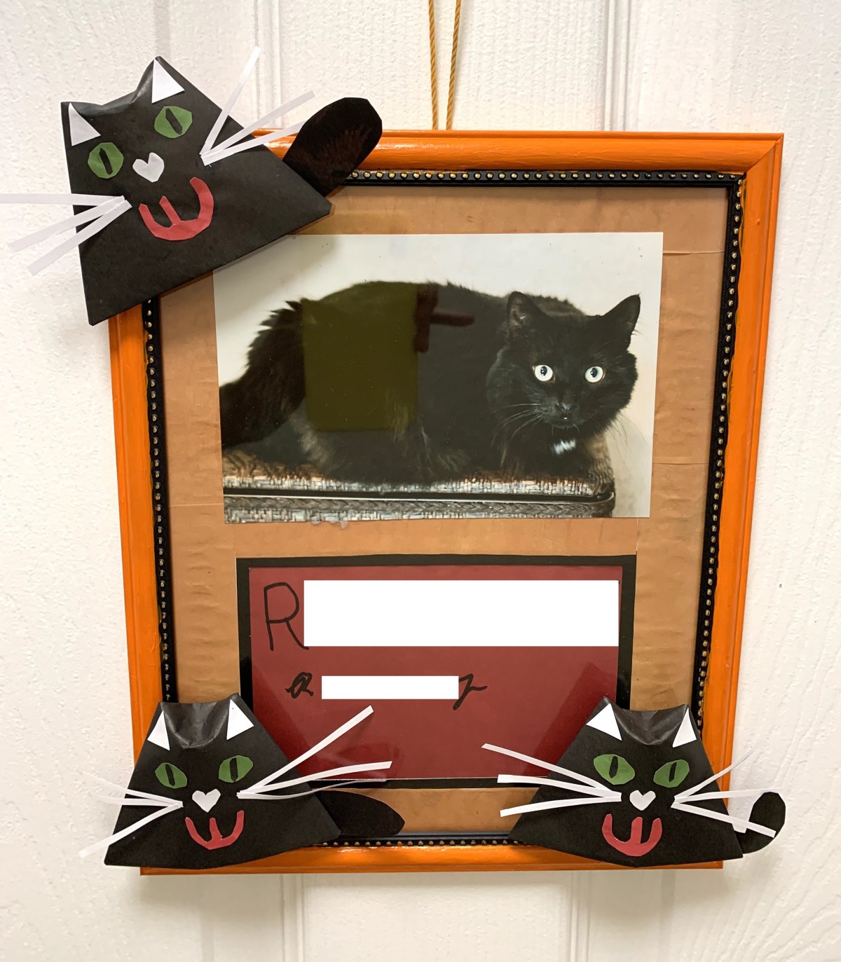 A framed photograph of a black cat surrounded by handmade cat decorations.