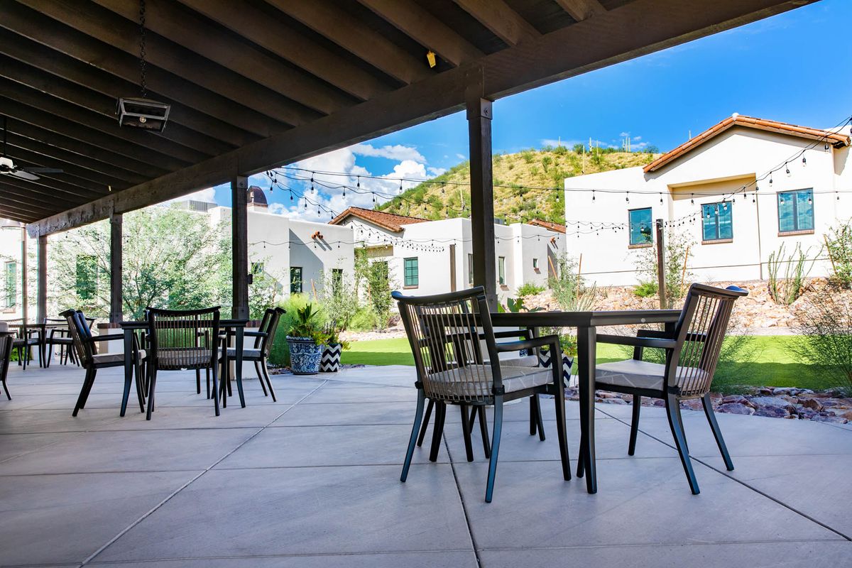 A covered outdoor patio with chairs and tables overlooking a residential area on a sunny day.