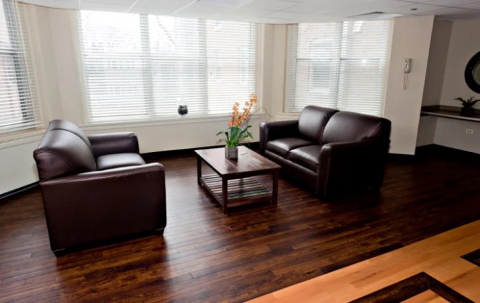 A minimalist living room with two leather sofas, a wooden coffee table, and large windows allowing natural light to fill the space.