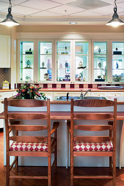 A cozy kitchen interior featuring a wooden counter with two chairs, decorated cabinets, and a window display.