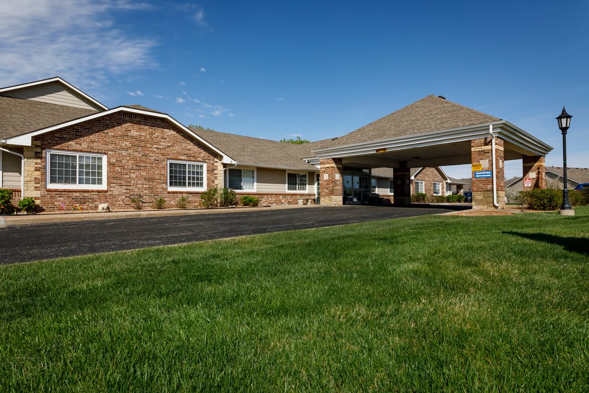 A brick building with a covered entrance surrounded by a well-maintained lawn under a clear blue sky.