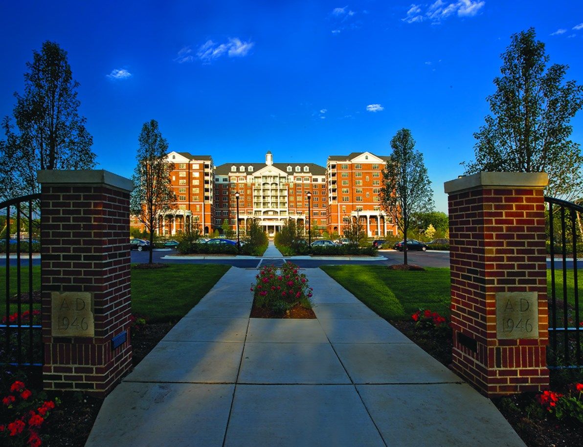 A grand brick building framed by a pathway and lush greenery under a clear blue sky.