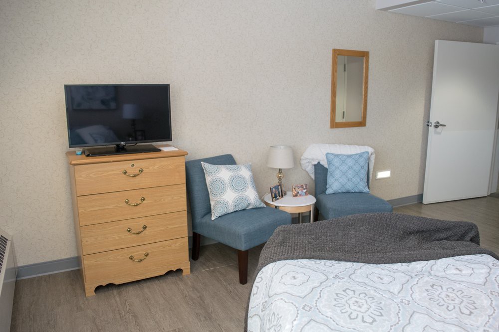 A cozy bedroom with two blue chairs, a wooden dresser, and a TV.