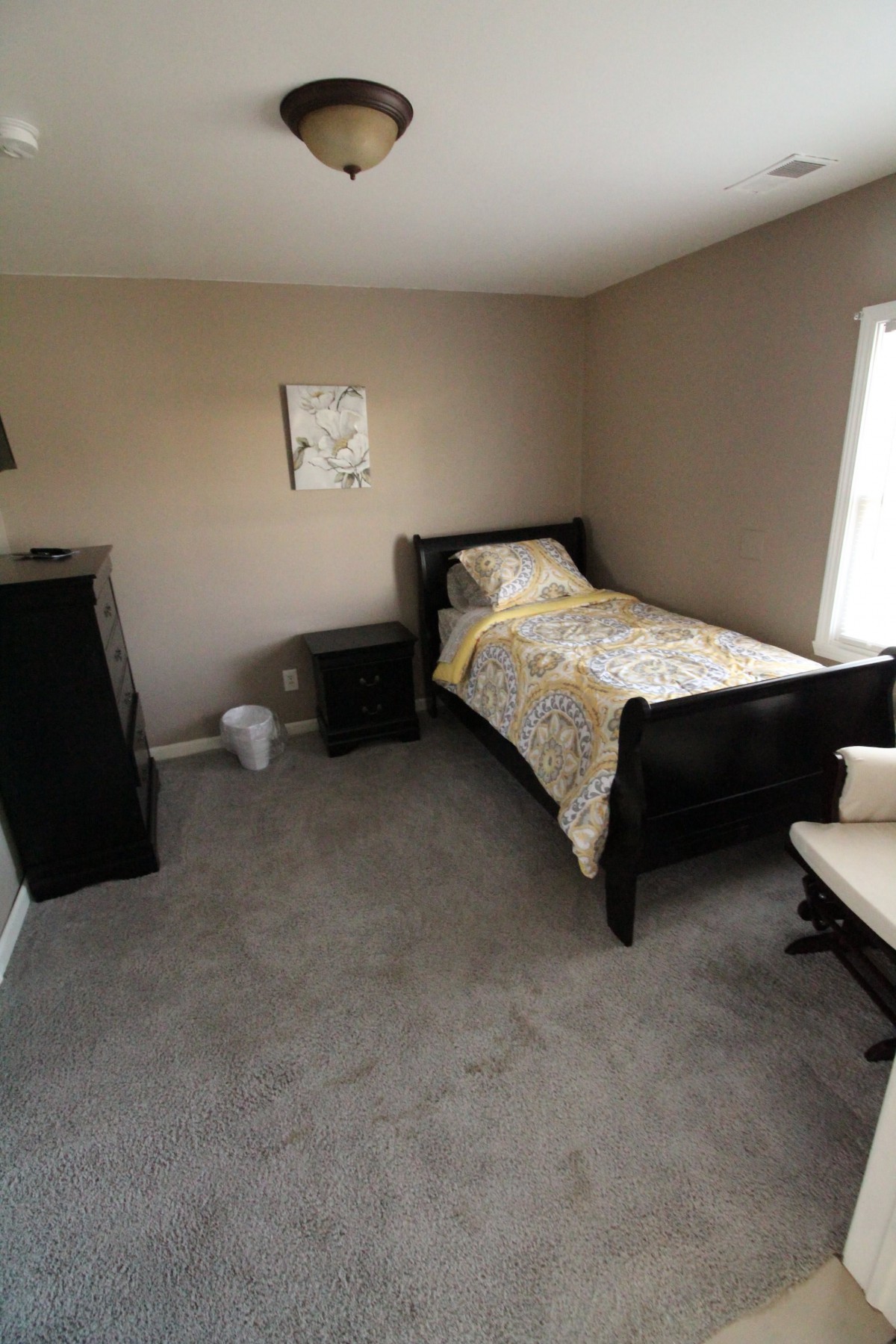 A cozy bedroom with a single bed, nightstand, and dresser featuring neutral tones.