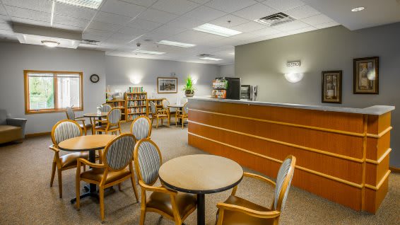 A reception area with tables and chairs, featuring a wooden desk and bookshelves.