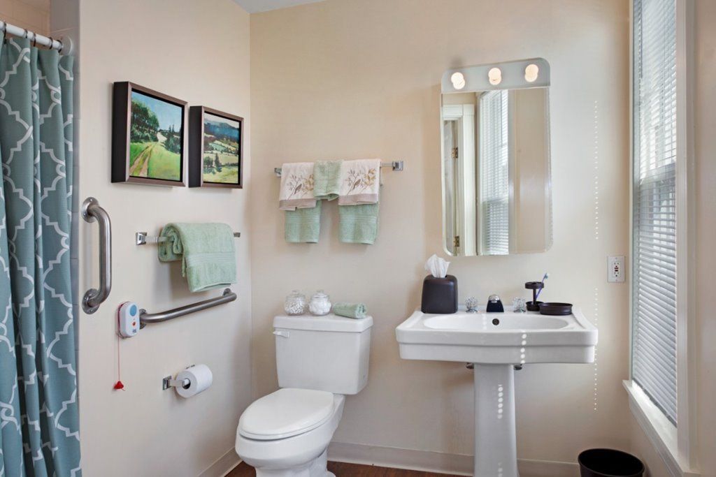 A well-organized bathroom with a pedestal sink, toilet, and wall mirror, complemented by green towels and framed artwork.