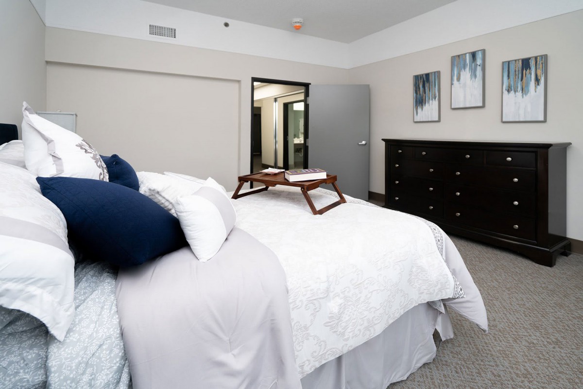 A cozy and neatly arranged bedroom with a comfortable bed, decorative pillows, a dresser, and a breakfast tray.