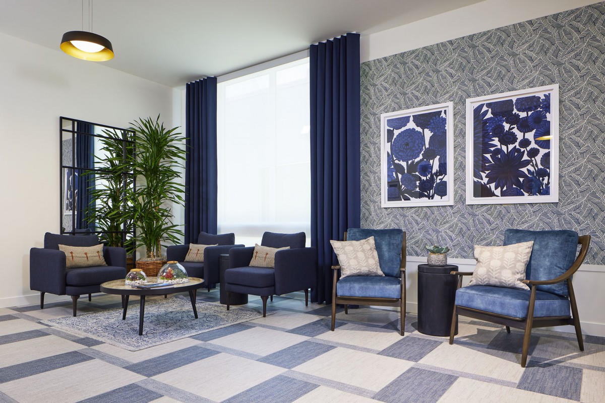 A modern living room featuring a blue and gray color scheme with stylish armchairs, a coffee table, curtains, wall art, and indoor plants.