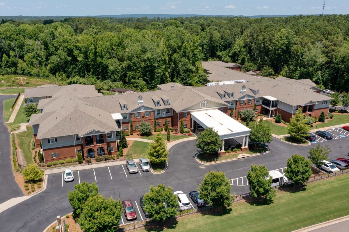 Aerial view of a building complex surrounded by trees with a parking lot and driveway in the foreground.
