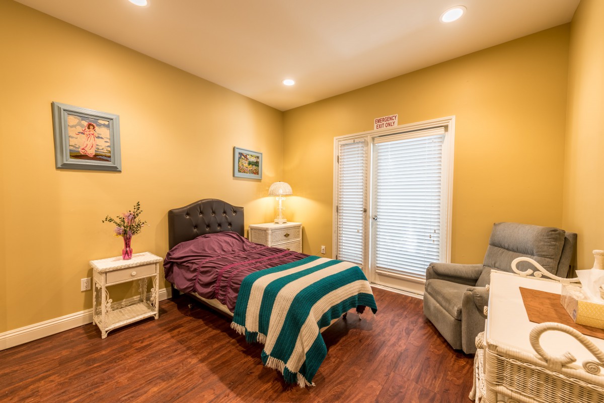 A cozy bedroom featuring a single bed with a striped blanket, nightstands with lamps, and an armchair on a hardwood floor.