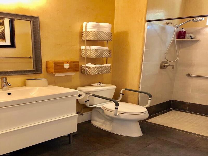 An accessible bathroom featuring a toilet with grab bars, a shower, and neatly organized towels on shelves.
