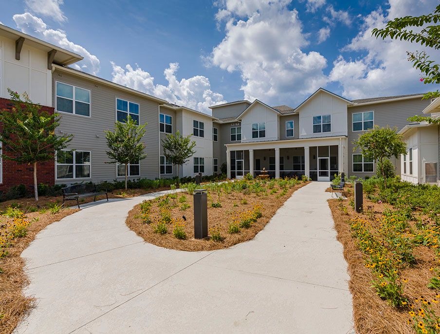 A modern residential building with landscaped pathways and a cloudy sky backdrop.