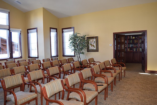 A spacious waiting room featuring several rows of comfortable chairs and natural light from large windows.