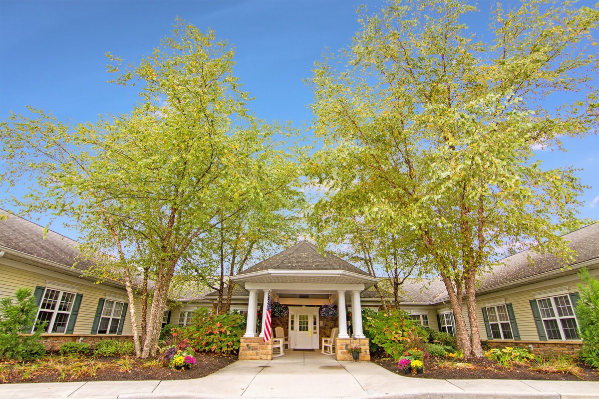 A welcoming entrance to a building surrounded by trees and landscaping on a clear day.