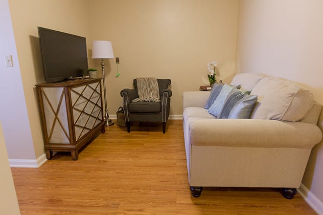 A cozy living room with a sofa, TV stand, armchair, and lamp.