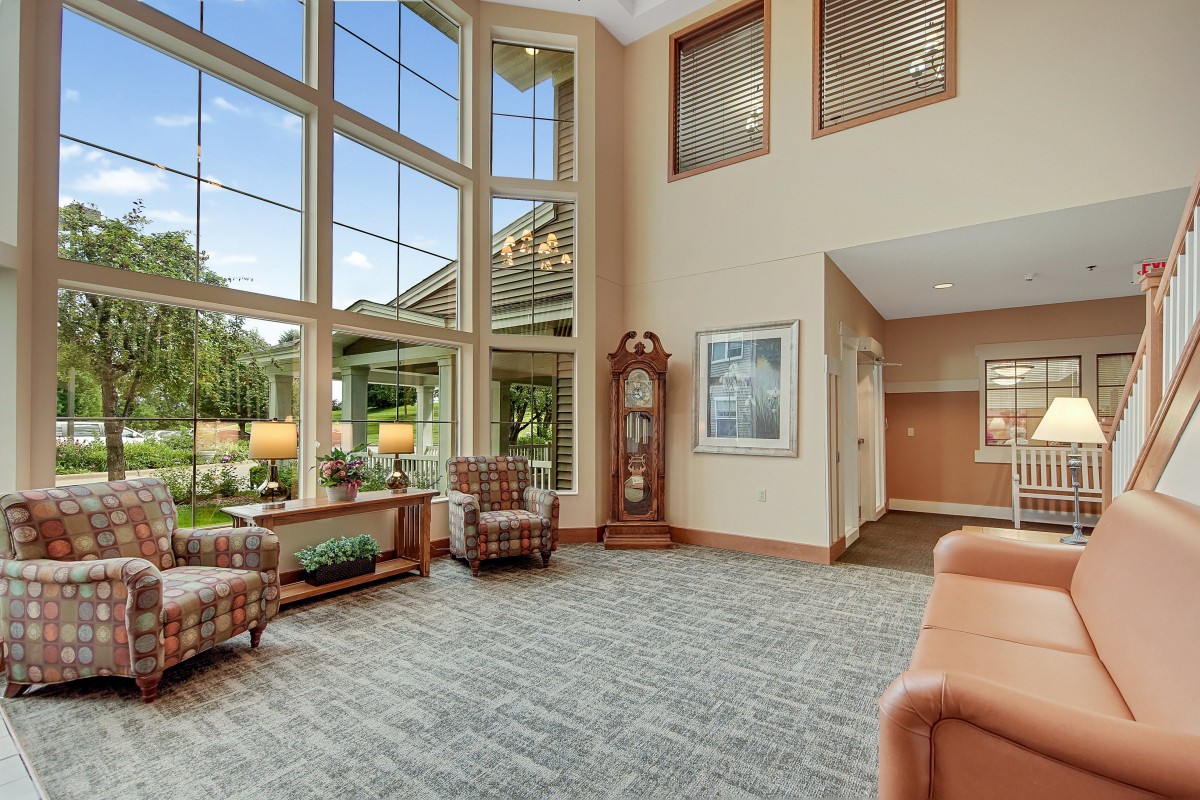 A spacious and bright lobby featuring large windows, comfortable seating, and a decorative clock.