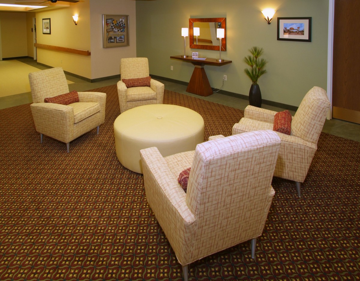 A cozy lounge area featuring a round ottoman surrounded by comfortable chairs with a mirror and plant for decor.