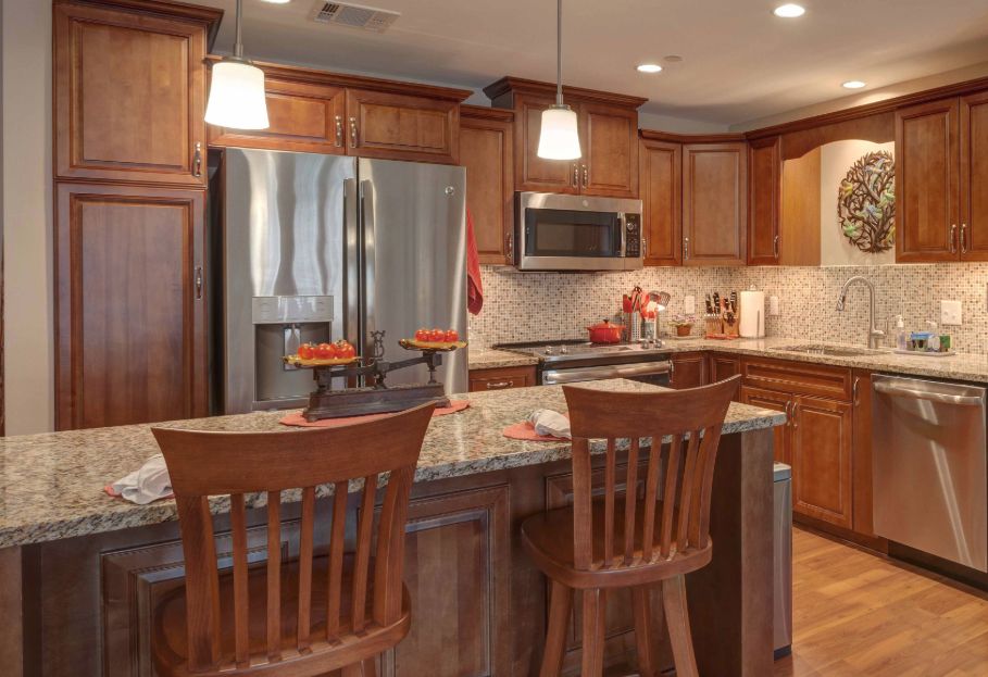 A modern kitchen with wood cabinetry, granite countertops, and island seating.