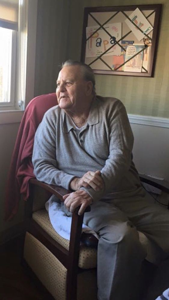 An elderly man sits by the window, looking out thoughtfully.