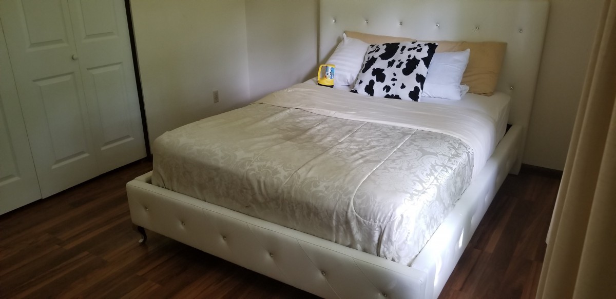 A neatly made bed with a white headboard and cow-print pillow in a simple bedroom setting.