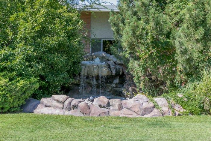 A small waterfall feature in a garden surrounded by lush greenery and rocks.