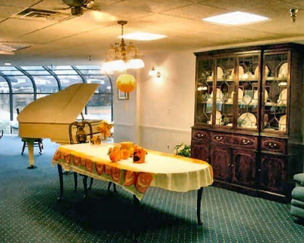 A cozy dining area featuring a grand piano, a decorated table with a yellow tablecloth and floral centerpiece, and an elegant china cabinet in a softly lit room.