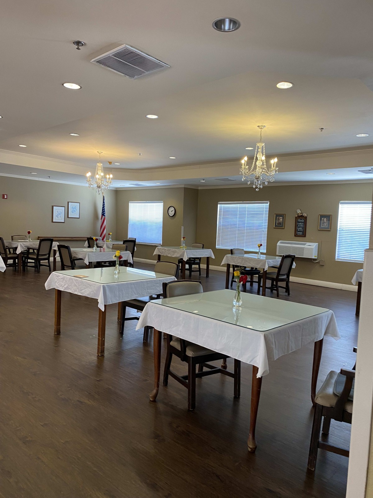 A well-lit dining room with neatly arranged tables covered in white tablecloths.