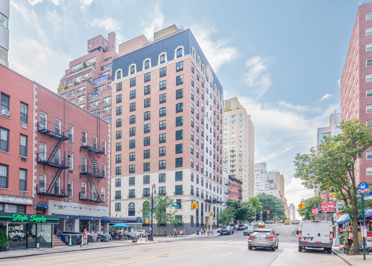 A vibrant city street with tall buildings and light traffic under a clear blue sky.