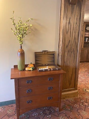 A cozy interior with a wooden chest of drawers adorned with a vase of flowers and a fruit arrangement.
