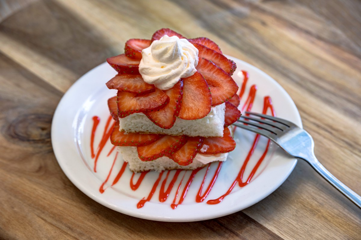 A delicious layered cake topped with fresh strawberries and whipped cream, served on a plate with strawberry syrup.