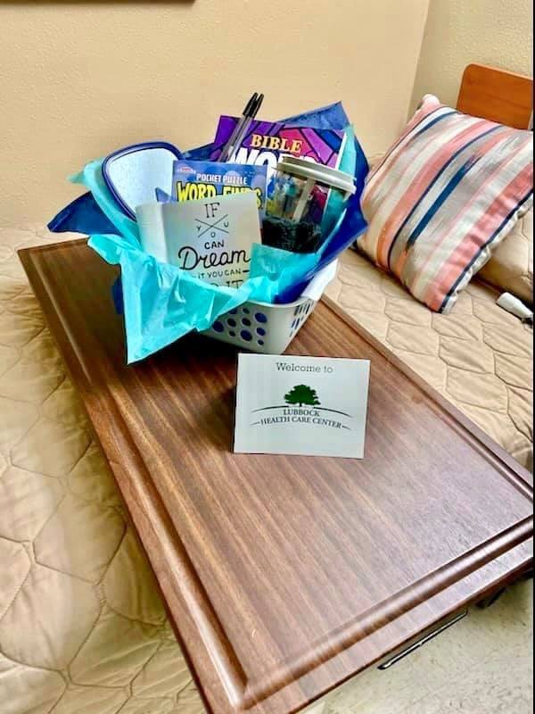 A cozy gift basket filled with books and goodies on a wooden tray in a bedroom setting.