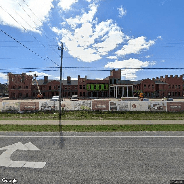 A partially constructed building behind a fenced area alongside a road under a cloudy sky.