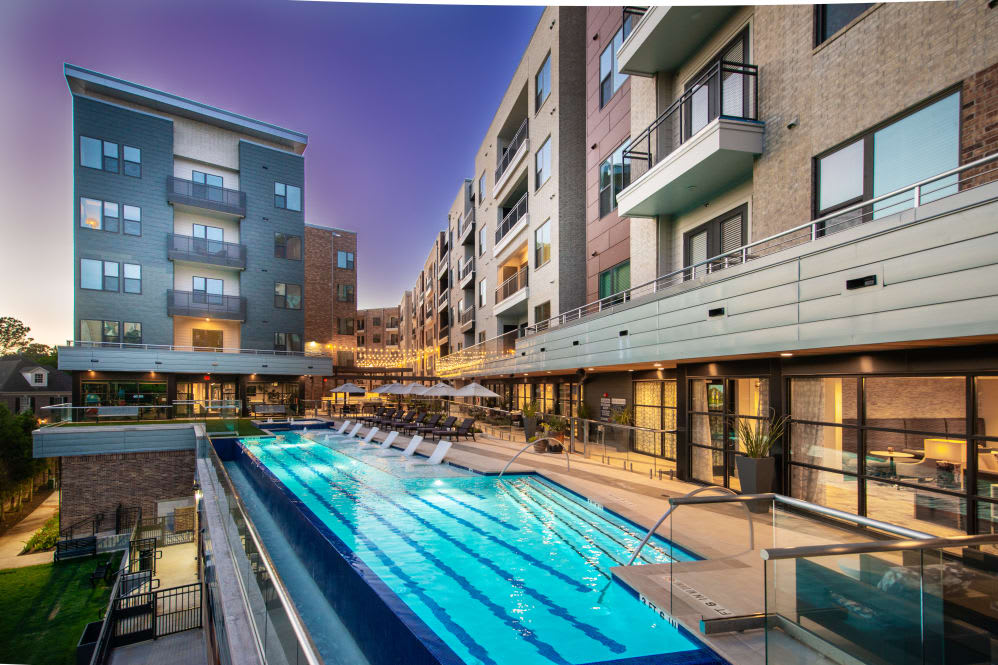 A modern apartment complex featuring an illuminated outdoor pool at dusk.