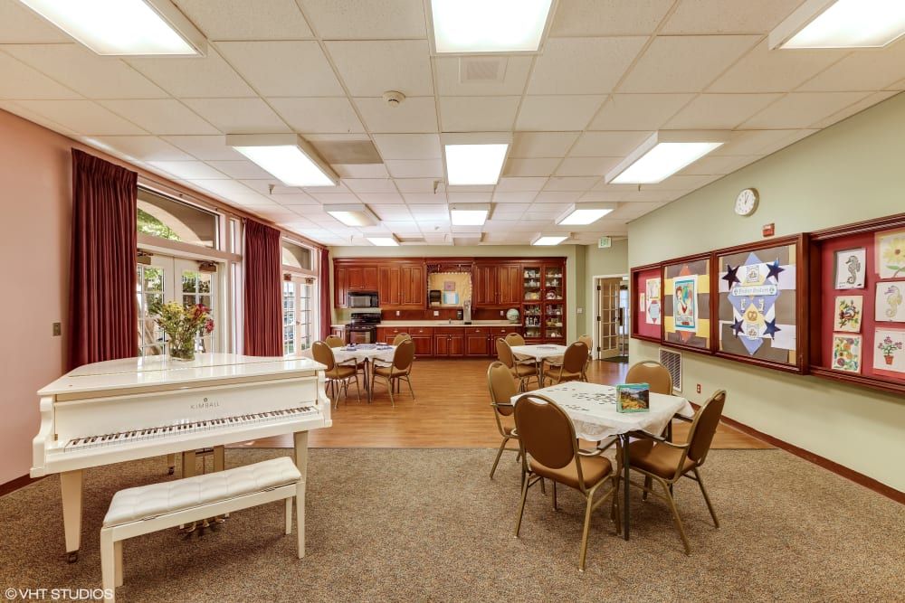 A cozy dining area with a piano, tables, and chairs adjacent to a kitchen.