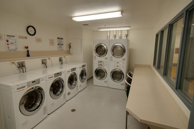 A commercial laundry room with washing machines and dryers lined up against the walls.