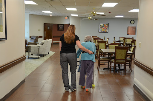 A caregiver assisting an elderly person as they walk together in a communal space.