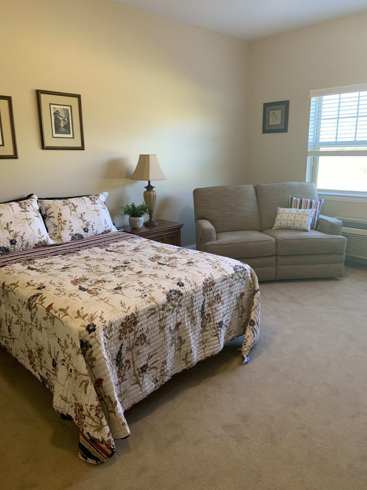 A cozy bedroom with a bed, sofa, and window allowing natural light.