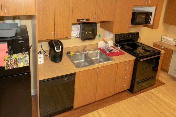 A compact kitchen with wooden cabinets featuring a double sink, coffee maker, dishwasher, stove, and microwave.
