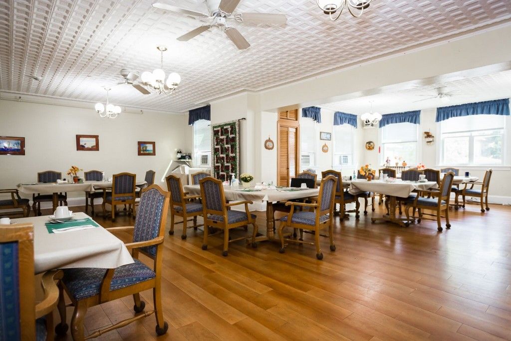 A spacious dining room with neatly arranged tables and chairs, featuring a wooden floor and ceiling fans.