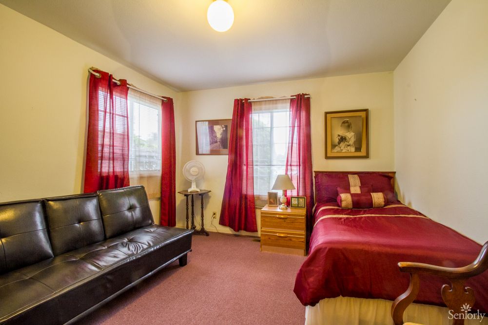A cozy bedroom with a bed, sofa, and vibrant red curtains.