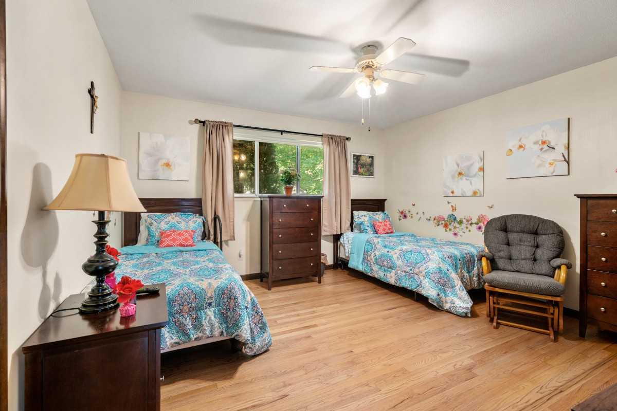 A cozy bedroom with twin beds, colorful bedding, and a ceiling fan.
