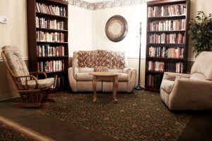 A cozy library corner with a sofa, armchair, and bookshelves filled with books.