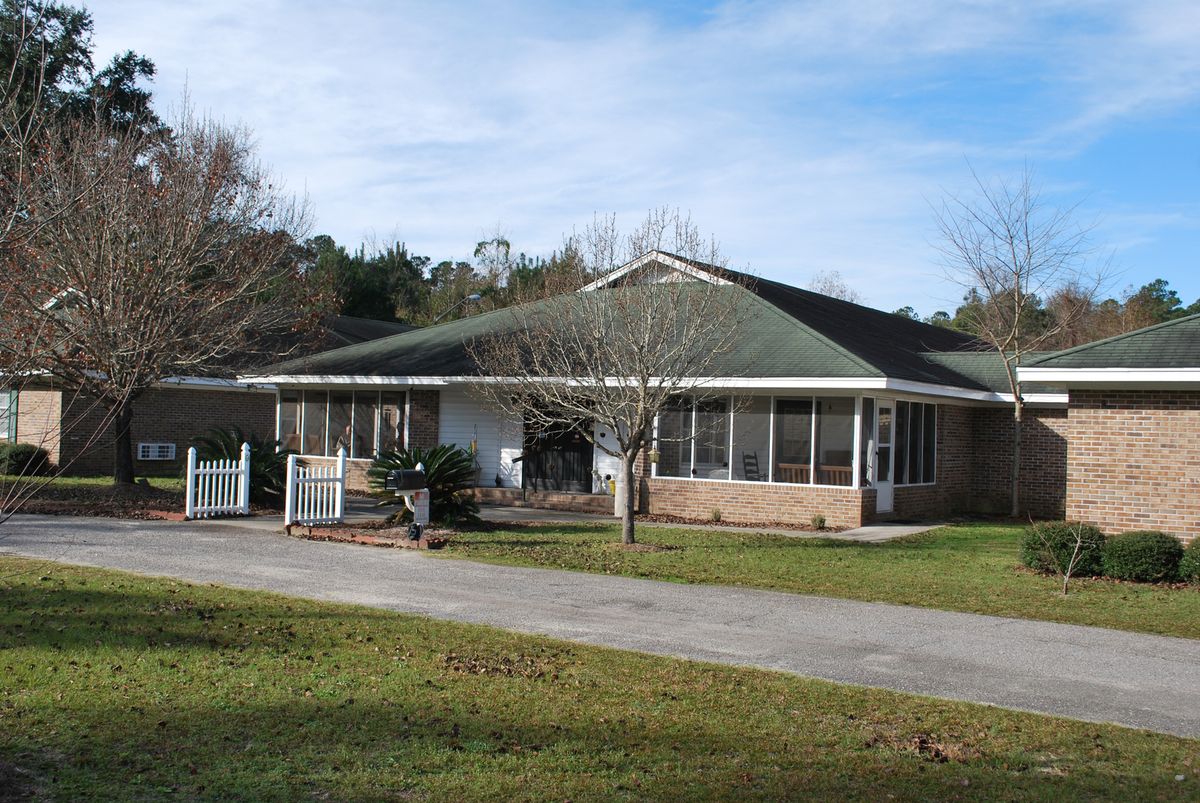 A single-story residential house surrounded by trees and a lawn.