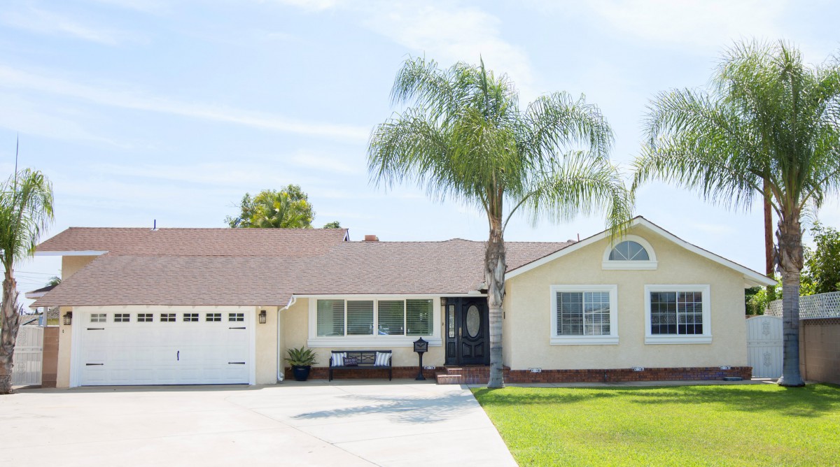 A suburban one-story house with a driveway and palm tree in the front yard.