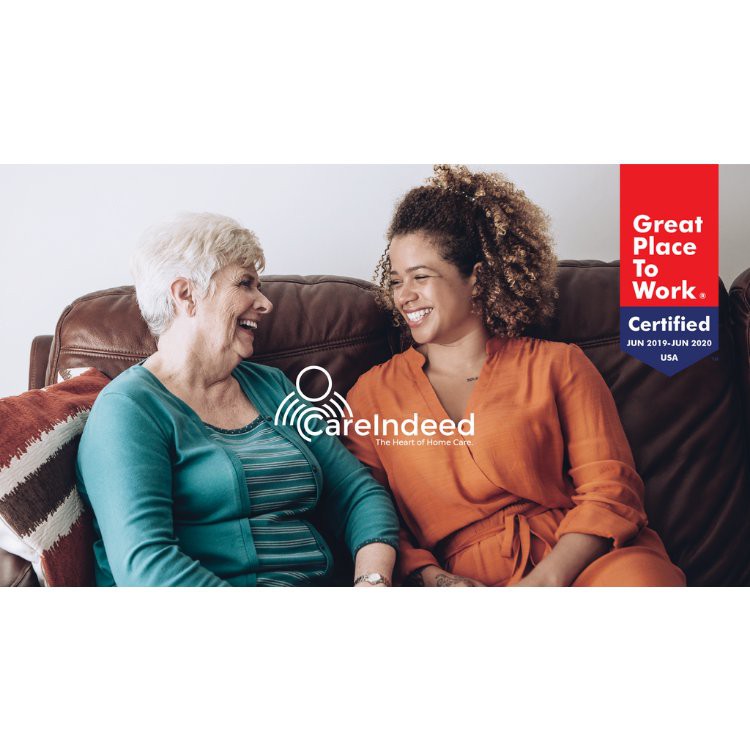 A caregiver and an elderly woman enjoying a warm conversation on a couch.