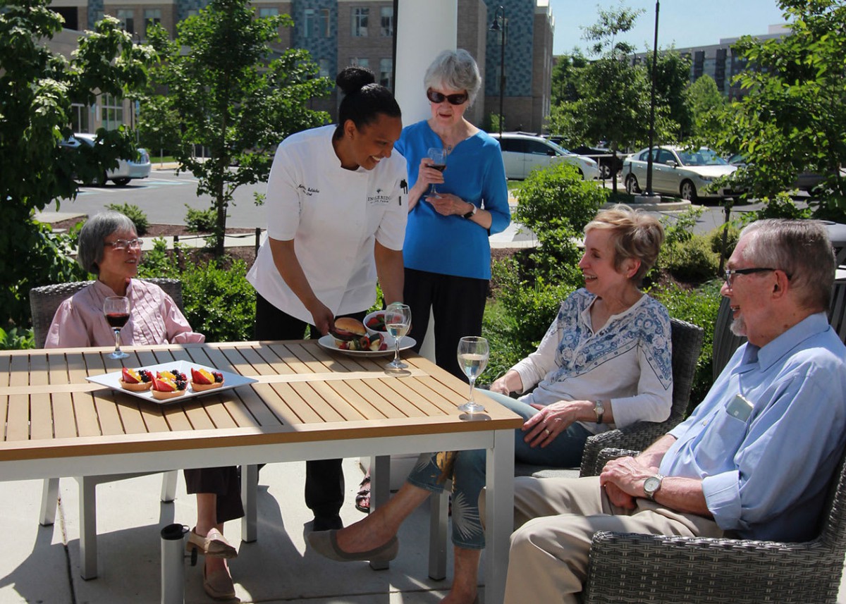 A group of seniors enjoying a social gathering outdoors, while a server attends to them on a sunny day.